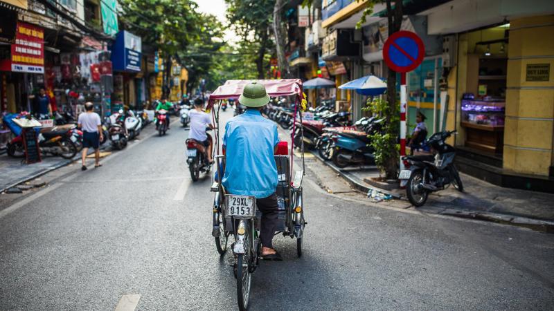 A lively street scene in a major Vietnamese city, showing diverse traffic with many modern cars.